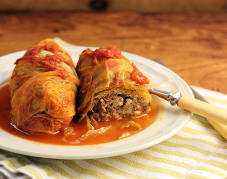 A plate of two cabbage rolls sitting in sauce. One of the rolls is cut open to show the meat and rice stuffing. A fork is stuck under one of the rolls and sticks out over the edge of the plate.