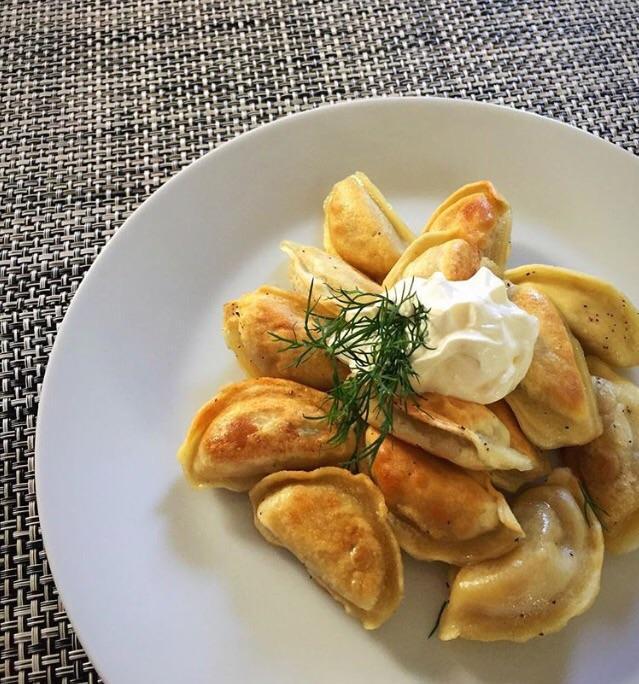 A plate of fried pierogi with a ramekin of sour cream and chives in the center